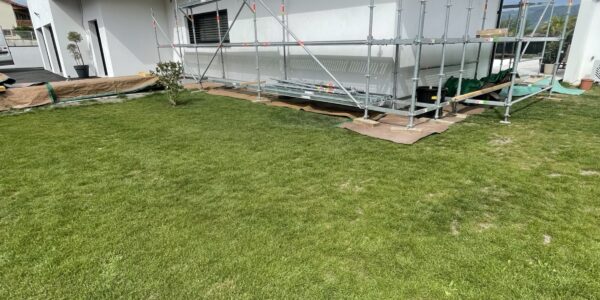Scaffolding set up along the side of a modern white house in a grassy backyard under renovation.